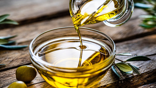 Olive oil being poured into a bowl on a table with olive leaves and fruit