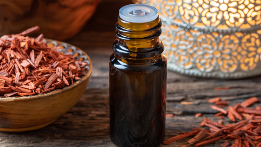Small amber glass bottle with stopper on a table with sandalwood chips and a lamp