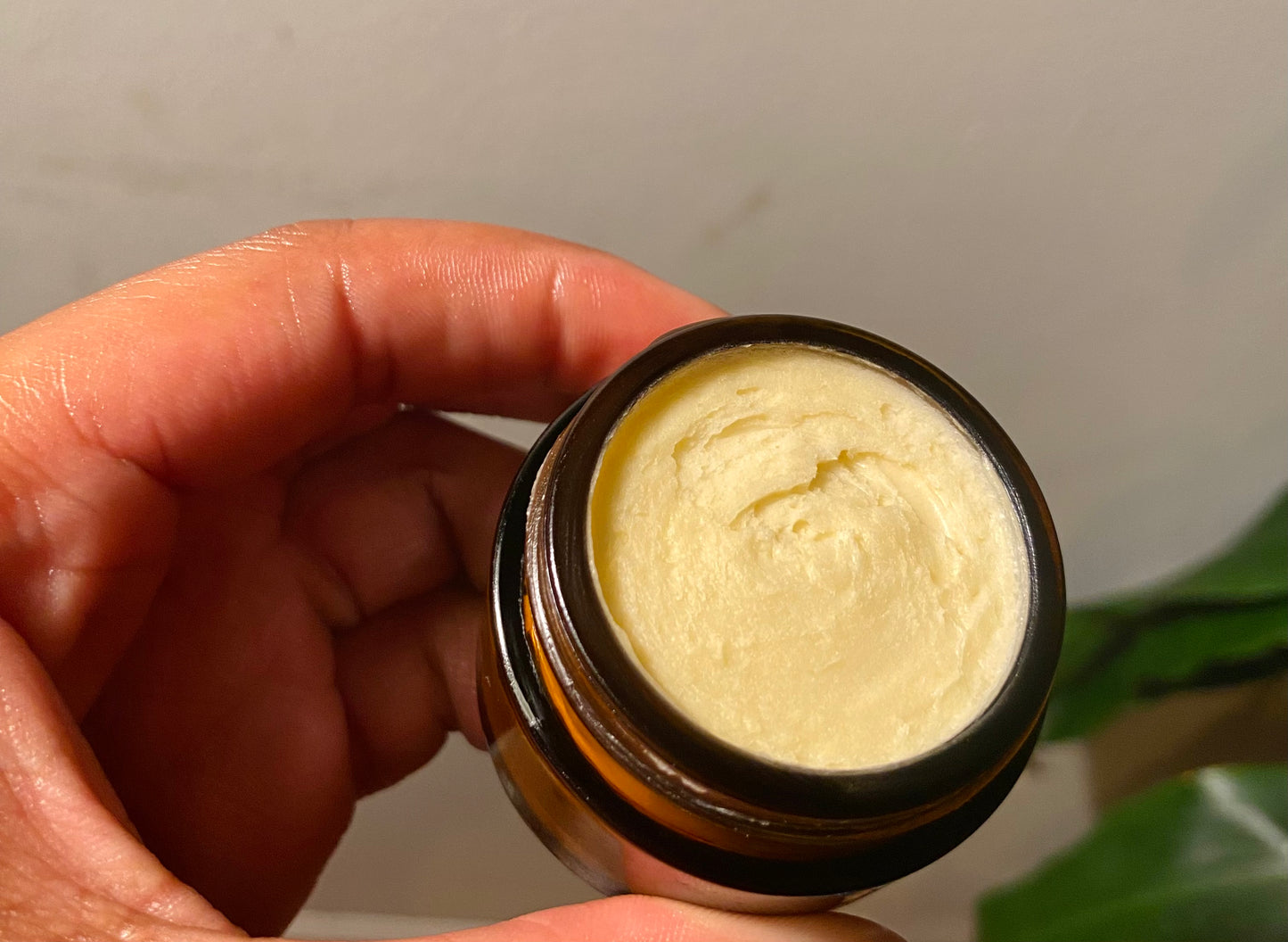 Hand holding shea butter for face in glass amber jar